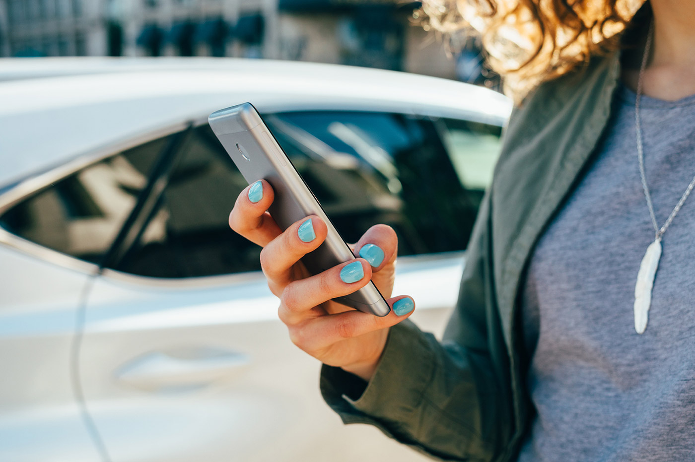 Woman texting on cell phone and standing in front of a car.