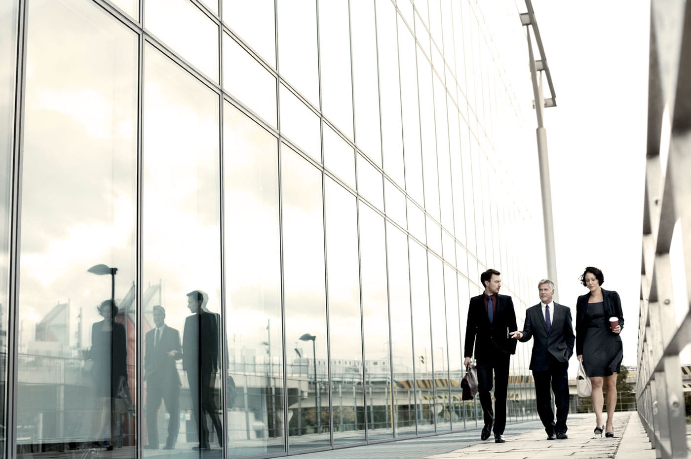 Three business people walking and talking while walking outside next to an office building.