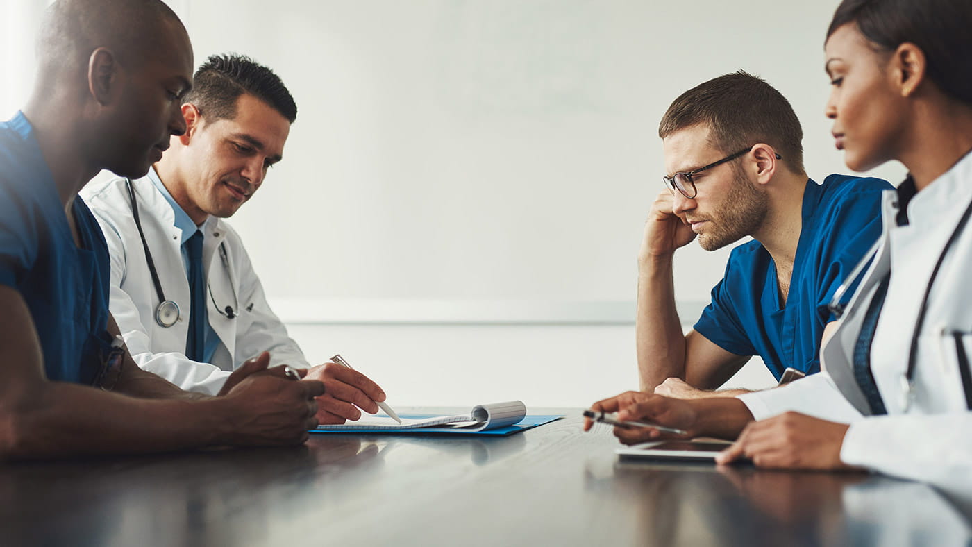 4 medical professionals sitting around a table looking at documents.