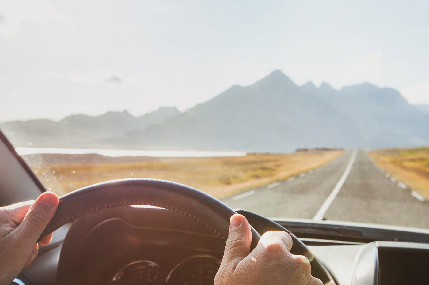 Steering wheel of a car driving down a road with mountains in the distance.