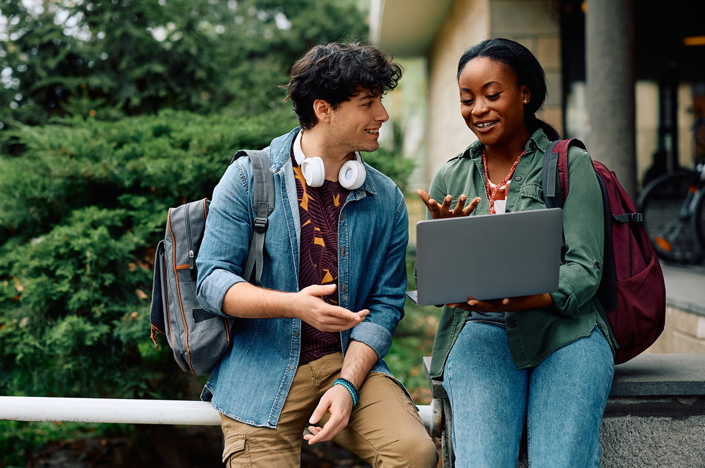 A woman and a man college students talking and one is holding an open laptop