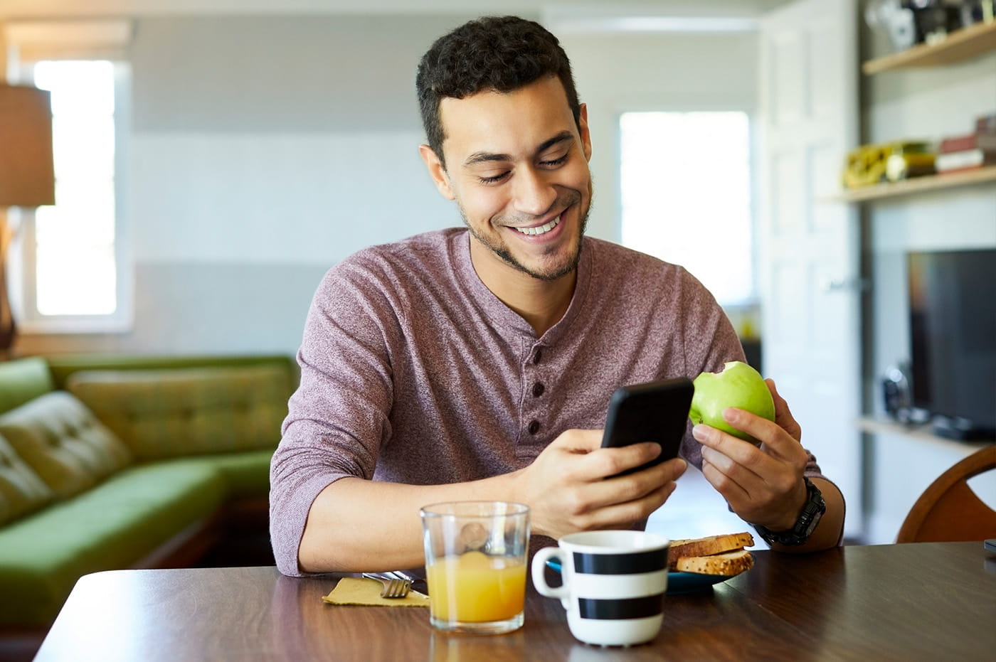 Man looking down at a cellular device and holding an apple. 