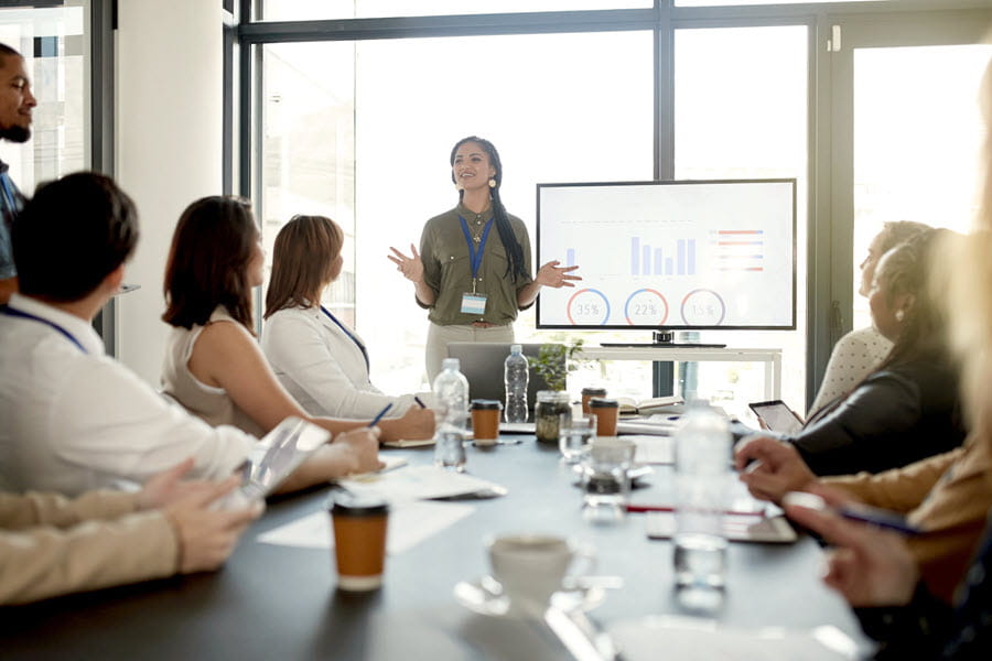 A woman standing and leading a large meeting.